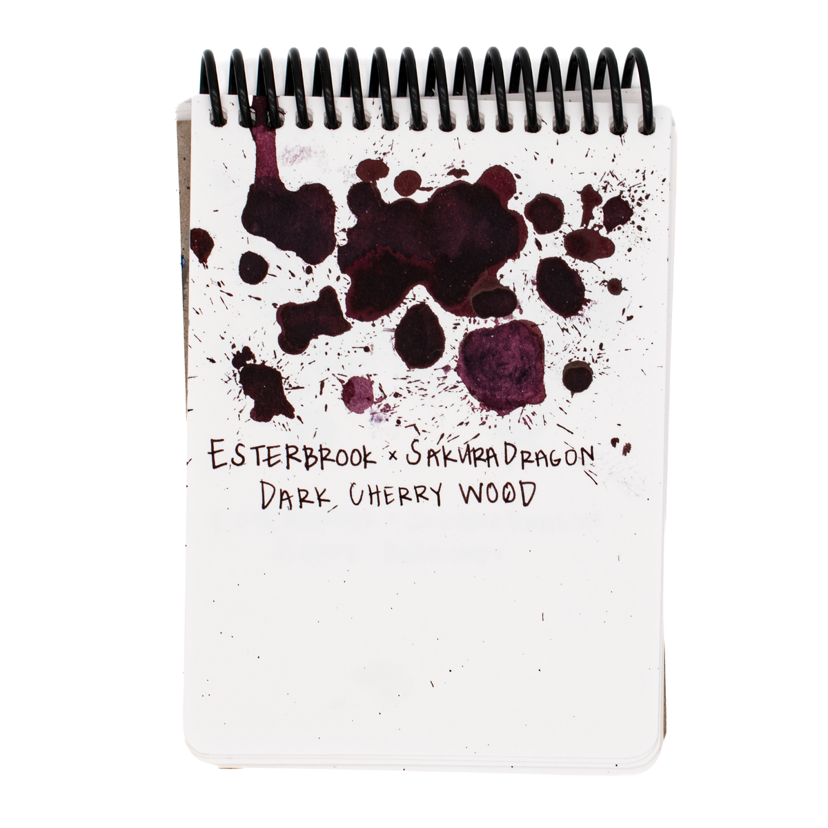 A spiral-bound notepad shown upright on a white background. The page is white with dark burgundy ink splatter graphics and handwritten text reading 'ESTERBROOK x SAKURADRAGON DARK CHERRY WOOD'.