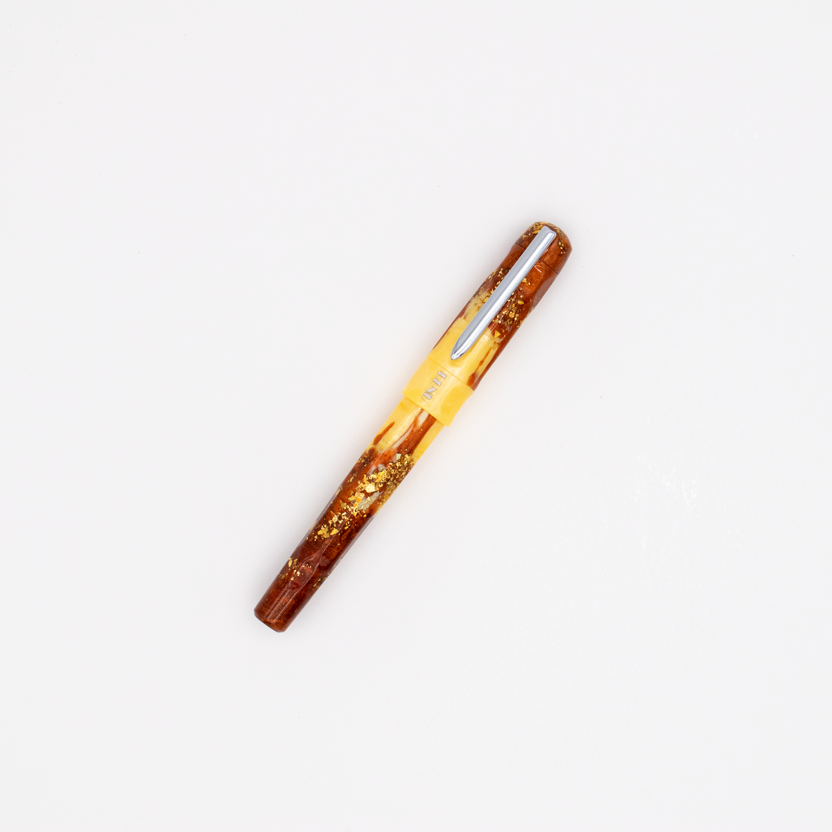A fountain pen with yellow and amber marble and gold flake accents with a silver nib and clip. The BENU logo is engraved with silver under the clip. The pen is photographed diagonally on a clean white background.