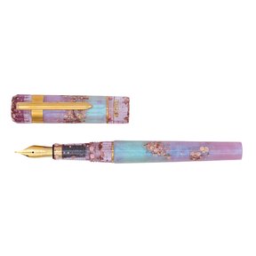 A translucent light blue and magenta pearly shimmer with chunky rose gold accents and gold trim with the cap posted on the barrel. The logo 'Benu' is engraved in gold on the bottom of the cap. The nib is gold with an ornate design engraving. The cap is parallel to the barrel on a white background. 