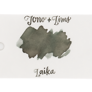 An ink swatch in a gray-green on white paper, with the text 'Tono+Lims' at the top and 'Laika' at the bottom in matching script on a plain white background.