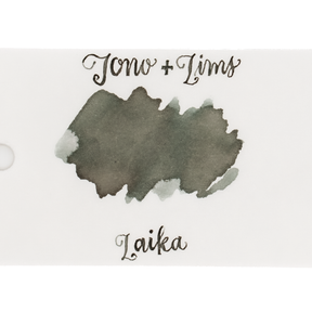 An ink swatch in a gray-green on white paper, with the text 'Tono+Lims' at the top and 'Laika' at the bottom in matching script on a plain white background.