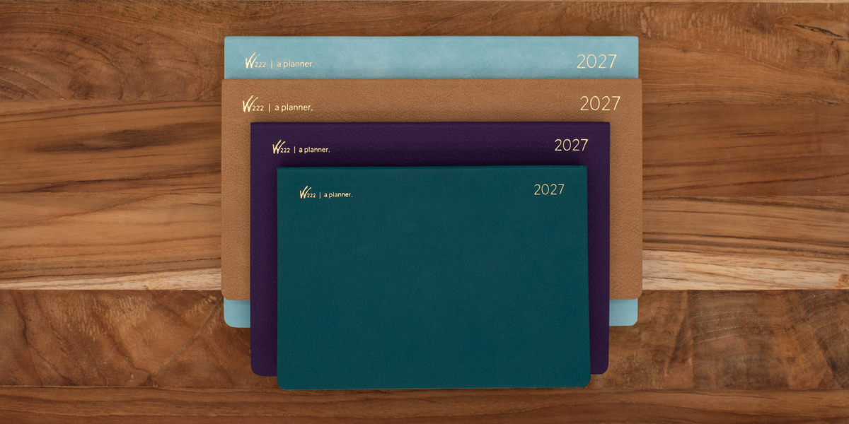 Four Wonderland 222 2027 planners stacked in glacial veil (pastel blue), coastal bluff (camel brown), ochre sea star (purple), and kelp forest (teal) with gold lettering, displayed on a wooden surface.